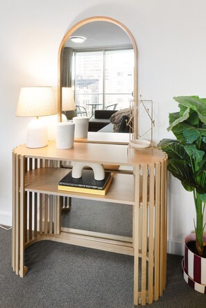 A wooden console table with a mirror, a lamp, a book, and a potted plant. - Central Eco-Luxe 2BR, 2BTH • Pool, Gym & Parking (Brisbane City)