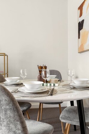 A dining table set with white plates, bowls, and glasses, accompanied by a vase and a candle holder. - Central Eco-Luxe 2BR, 2BTH • Pool, Gym & Parking (Brisbane City)