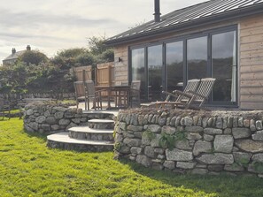 A modern house with a stone wall, a wooden deck, and outdoor seating. - Granfers (Penryn)