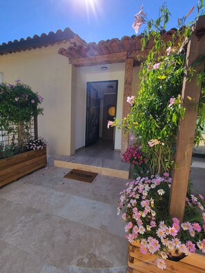 A welcoming entrance with a 'WELCOME' mat, a wooden pergola with flowers, and a tiled pathway leading to a door. - Large, modern villa consisting of 4 fully equipped, independent apartments (Saint-Paul-de-Vence)
