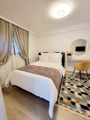 A modern bedroom with a bed, a desk, a chair, a mirror, and a patterned rug. - Large, modern villa consisting of 4 fully equipped, independent apartments (Saint-Paul-de-Vence)