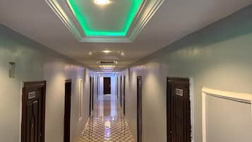 Pasillo de hotel con piso a cuadros, puertas a ambos lados y techo iluminado en verde.