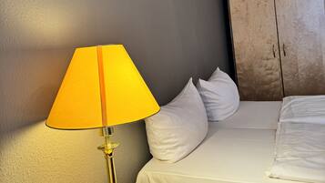 Habitación de hotel con cama, mesita de noche con lámpara, armario de madera y espejos en la pared.