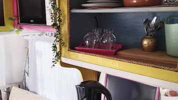 Uma cozinha compacta com micro-ondas, prateleiras com louças, cafeteira e uma pequena planta.