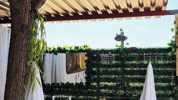 Un espacio exterior cubierto con un árbol, un banco y una pared con vegetación y una cerca de metal.