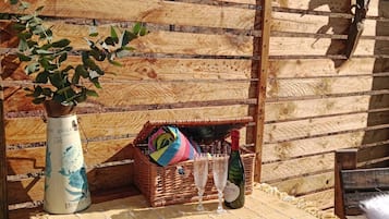 Un banco de madera con un tapete tejido, un florero con una planta, una cesta de mimbre y una botella de vino.