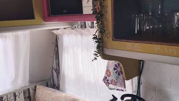 A compact kitchen with a microwave, a kettle, and a shelf with dishes.