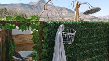 A wooden deck with a metal chair, a white towel hanging on a metal rack, and a metal showerhead.