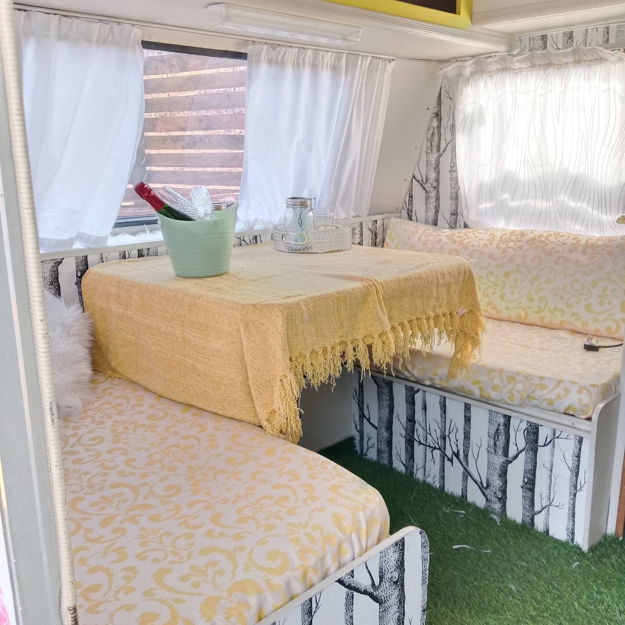 Un intérieur chaleureux avec un canapé et une table, une fenêtre avec des rideaux et un mur orné d’un motif d’arbre.