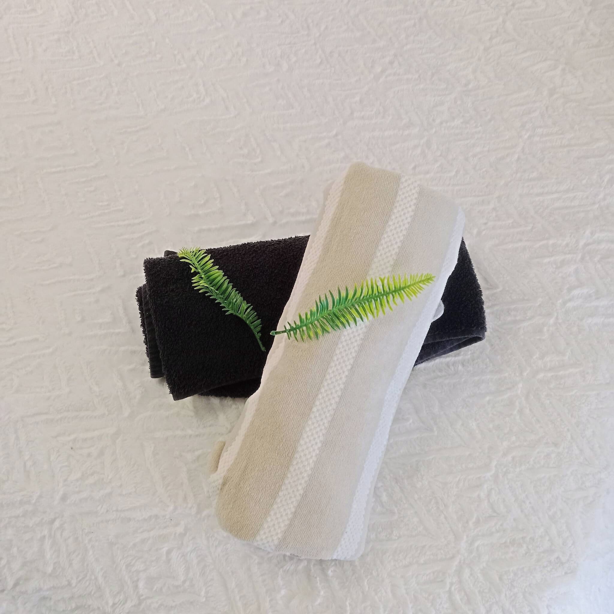 A rolled towel with a green leaf decoration on a textured white surface.