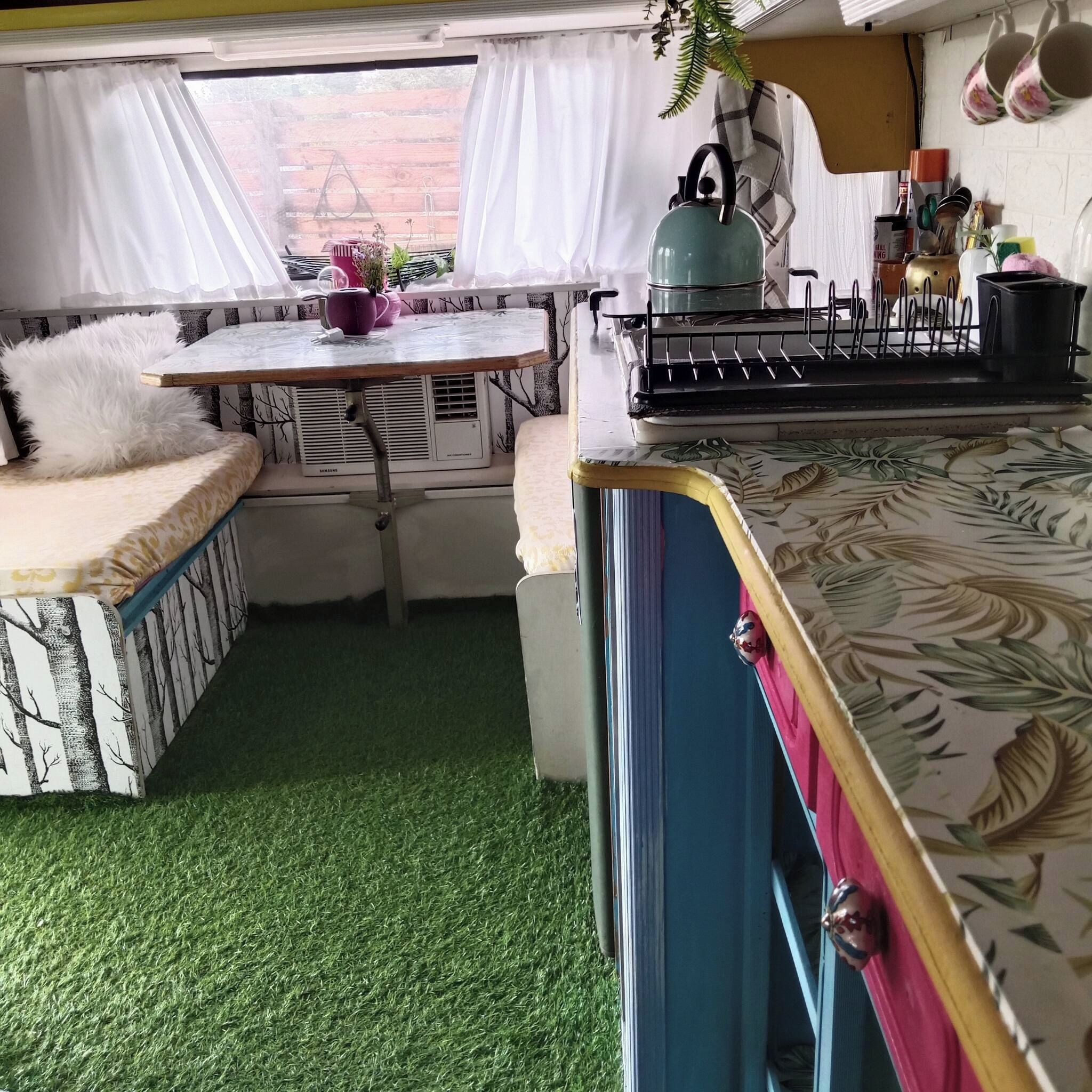 Een kleine keuken met een eethoek, een vloer van kunstgras en een raam met gordijnen.