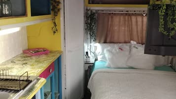 A compact room with a bed, a small desk, a refrigerator, and a window with curtains.