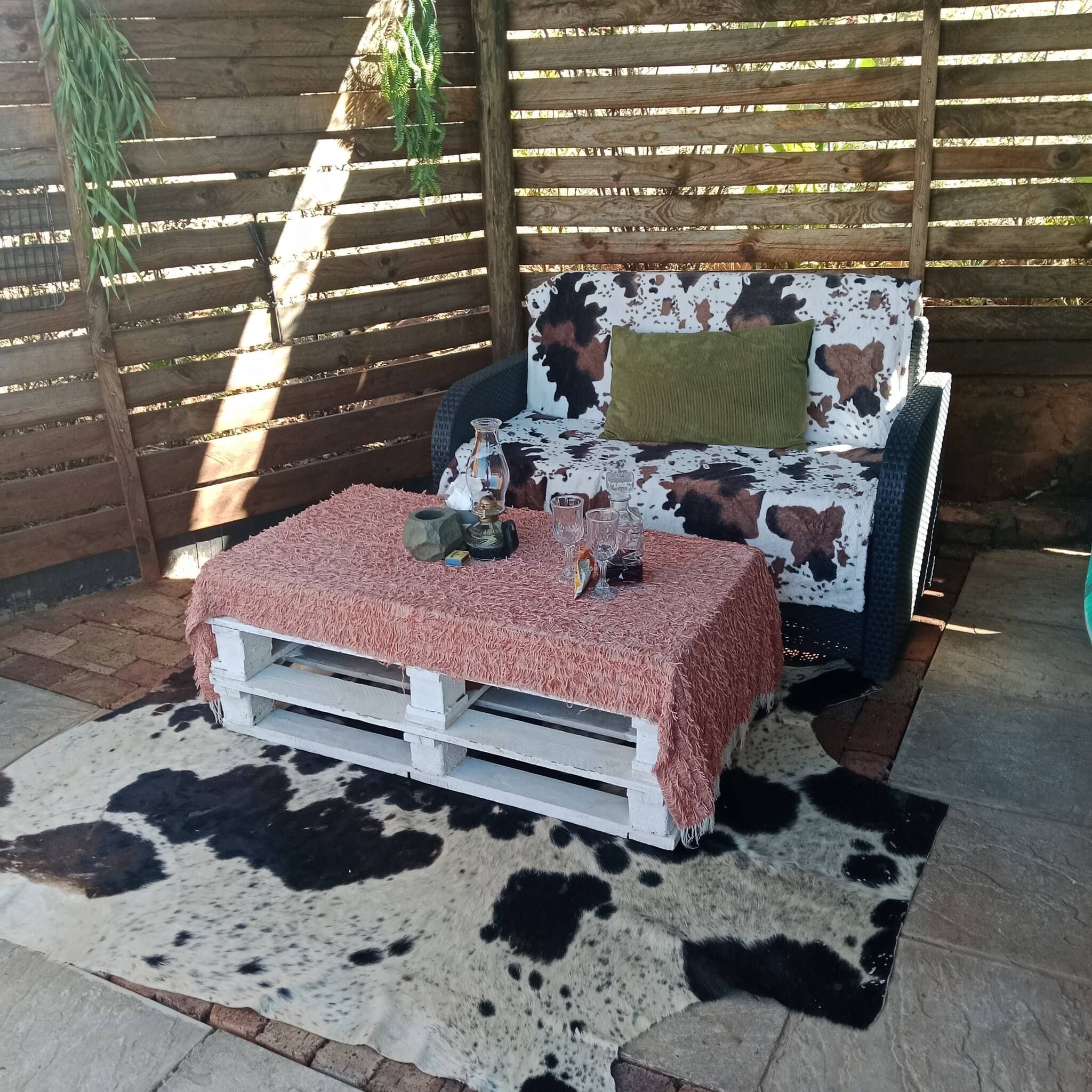 Un espacio al aire libre acogedor con alfombra de vaca, un banco blanco y un sofá estampado.