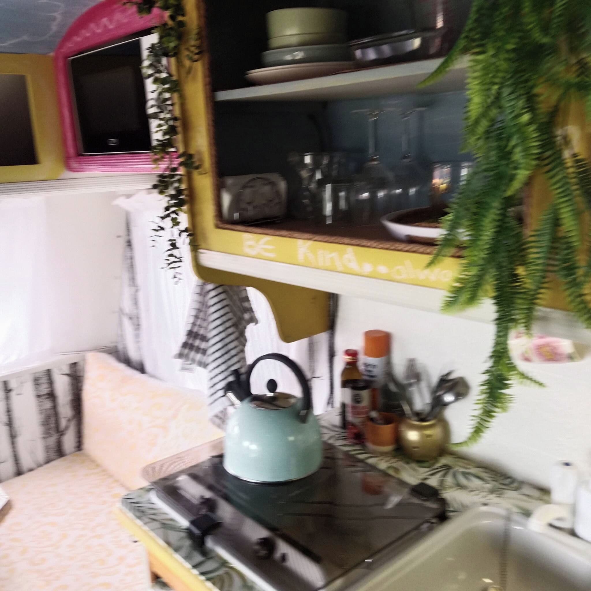 Une cuisine équipée d’une cuisinière, d’un évier et d’une étagère où sont rangés les ustensiles de cuisine.