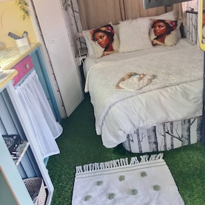 A bedroom with a bed, a bedside table, a wardrobe, and a small rug. - Romantic Clarens Getaway - Glamped Caravan With Braai & Fairy Bath (Clarens)
