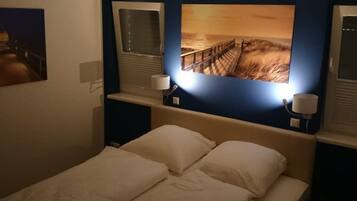 Habitación de hotel con una cama, dos lámparas de noche y un cuadro grande de una puesta de sol sobre el océano.