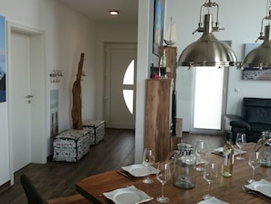 A dining area with a wooden table set for a meal, a large pendant light, and a view of a living room with a sofa. - "captain Dornfelder" (Trent)