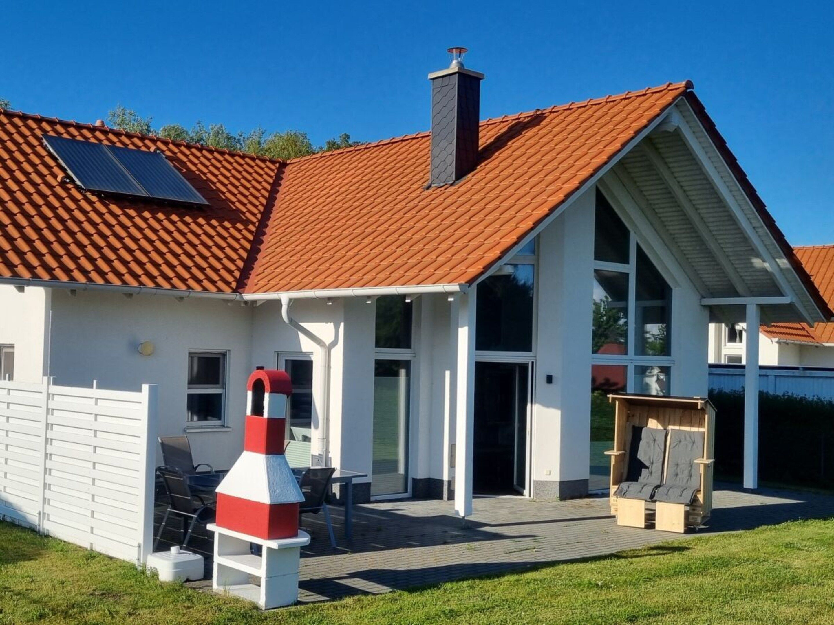 Una casa moderna con tejado de tejas rojas, una chimenea y un espacio al aire libre cubierto con una mesa y sillas.