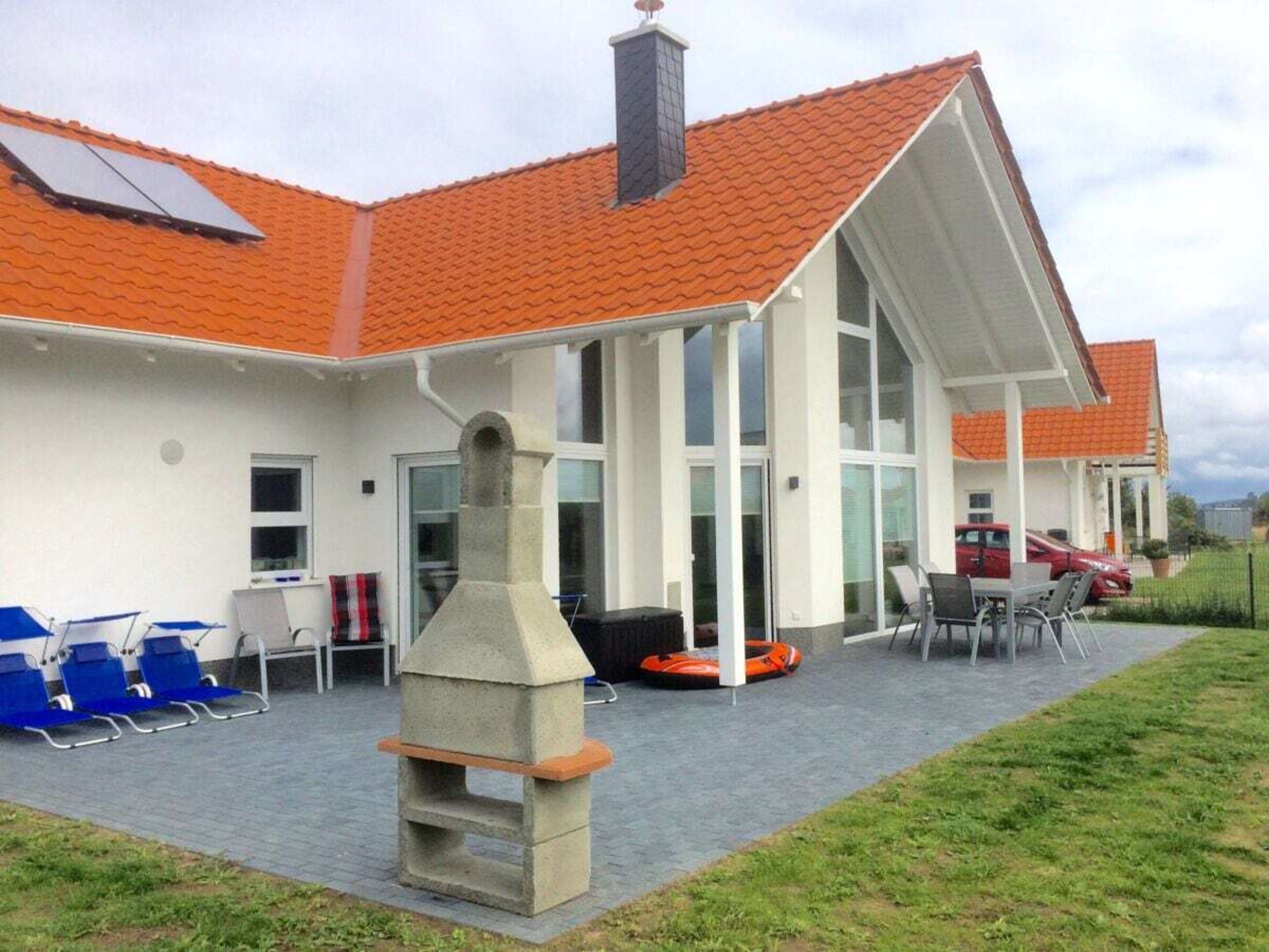 Un edificio con techo de tejas, un patio cubierto con mobiliario y una chimenea.