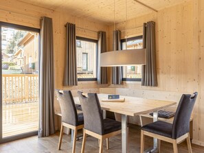 A wooden interior with a dining table and chairs, large windows with curtains, and a view of the outside. - Cabin With 1 Bedroom (Sankt Georgen am Kreischberg)