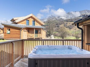 Uma cabana de madeira com hidromassagem em um deck, com vista para uma paisagem montanhosa.