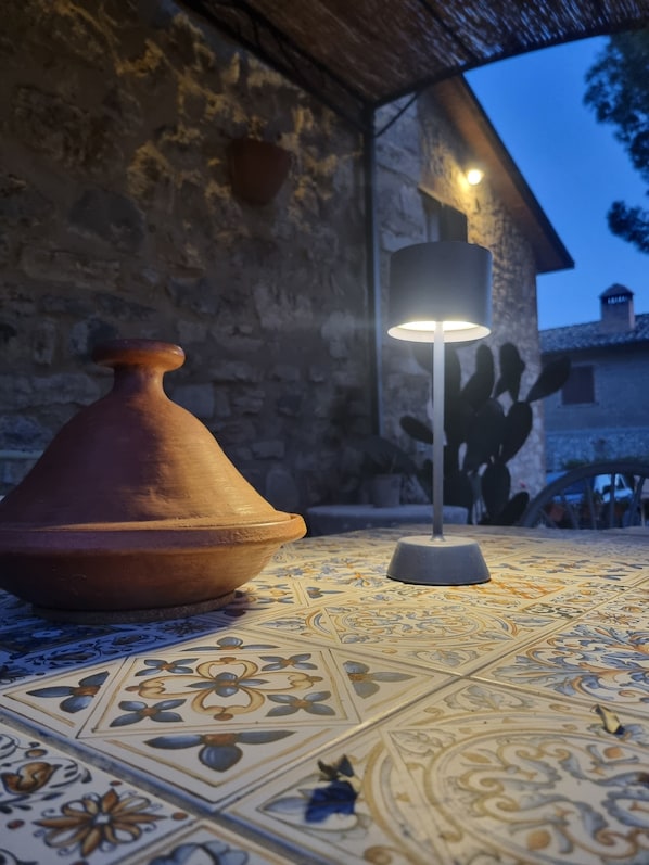 Una maceta de terracota y una lámpara moderna sobre un suelo estampado, con una pared de piedra y un edificio al fondo.
