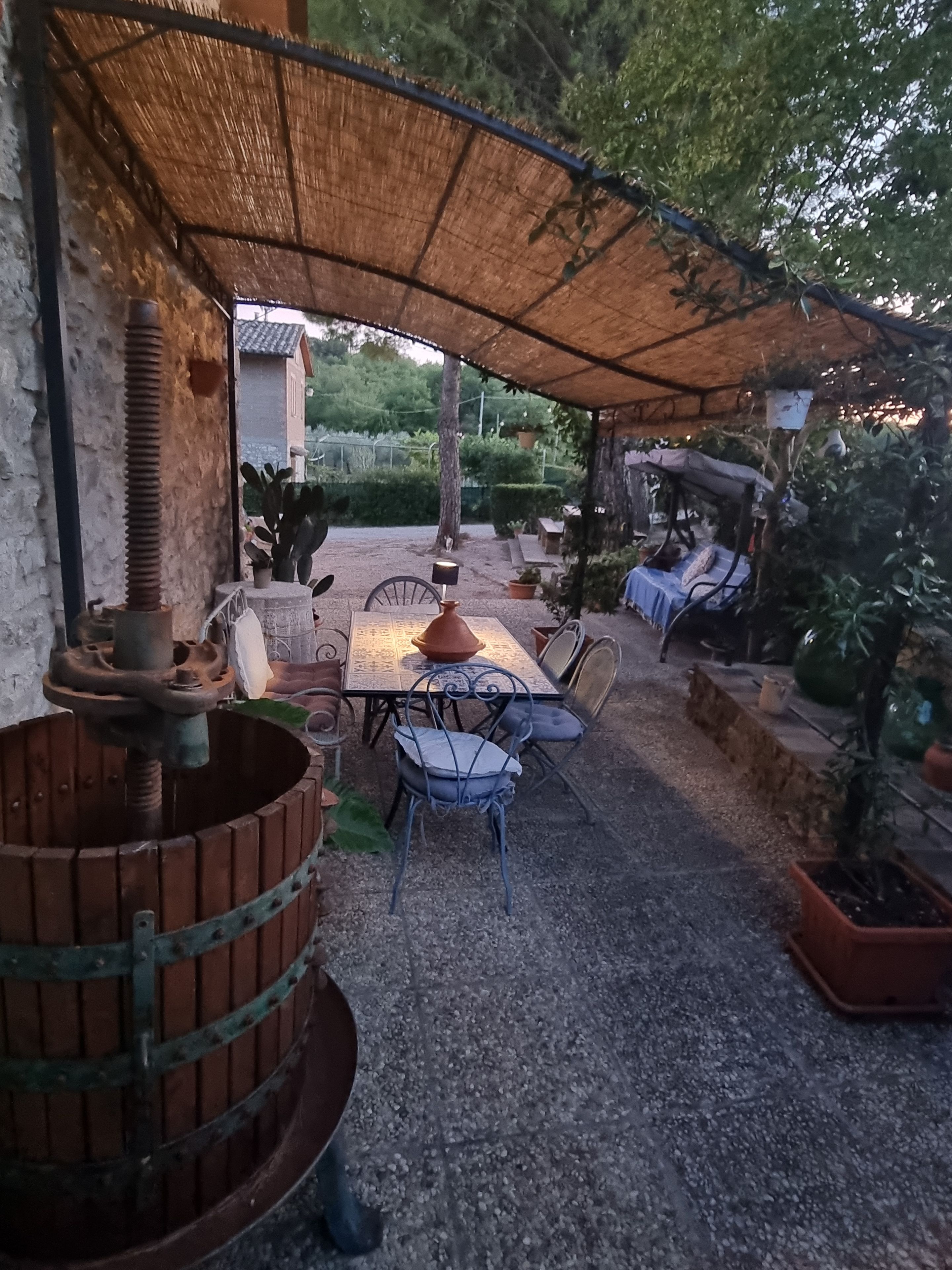 An outdoor patio with a table and chairs, surrounded by potted plants and a rustic water feature.
