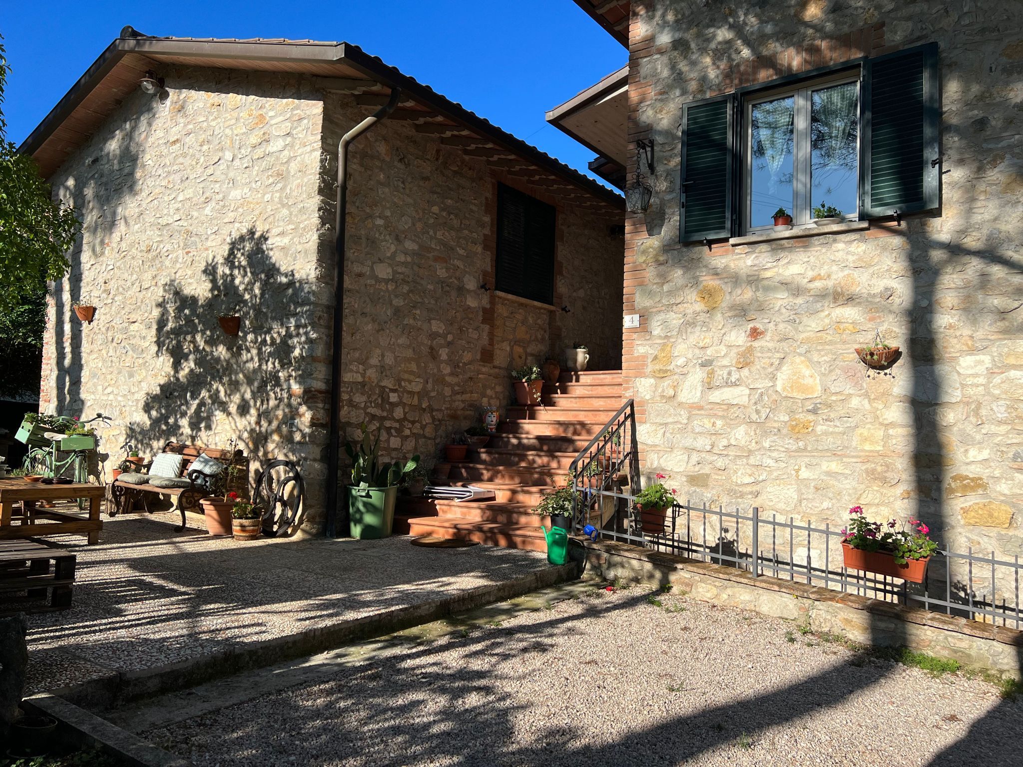 Un edificio in pietra con una scala che conduce al secondo piano, circondato da ghiaia e piante in vaso.