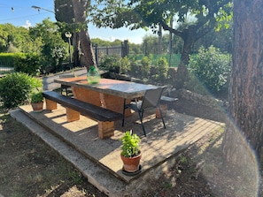 Een buitenpatio met een stenen tafel, bankjes en een plant in een pot.