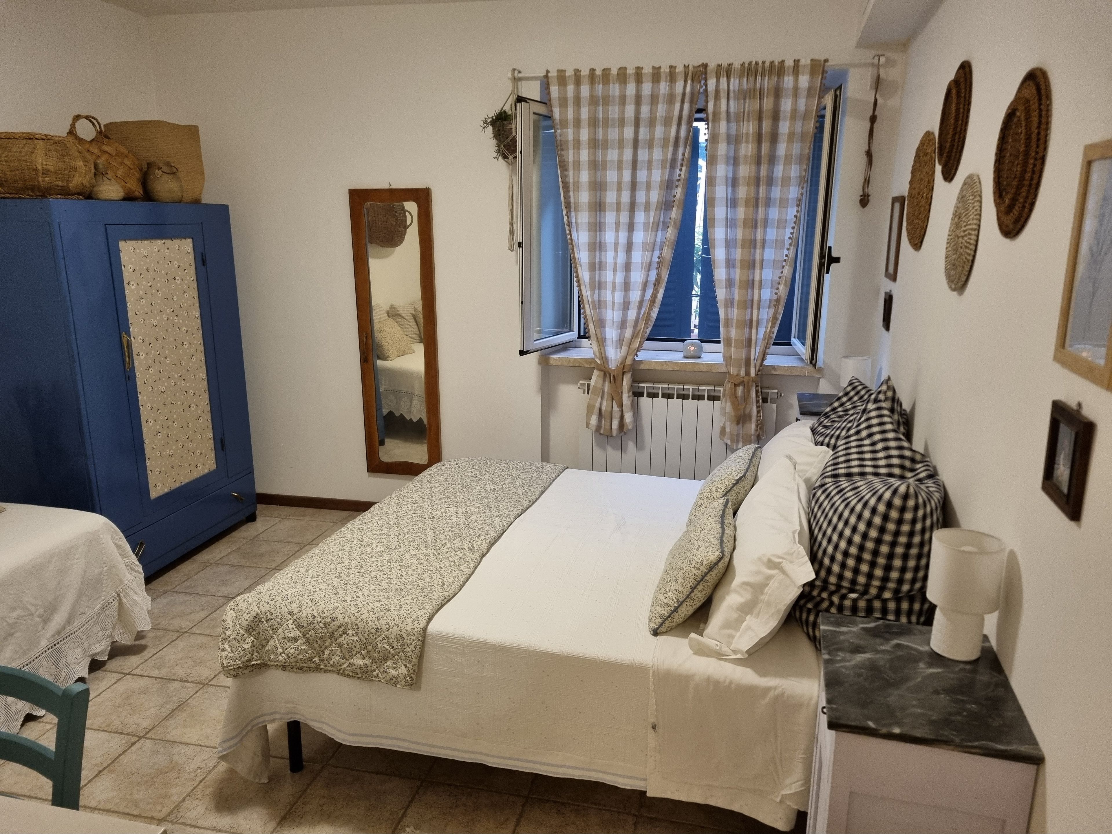 Una camera da letto con un letto, un armadio blu, uno specchio, una finestra con tende e un termosifone.