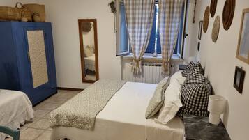 Una camera da letto con un letto, un armadio blu, uno specchio, una finestra con tende e un termosifone.
