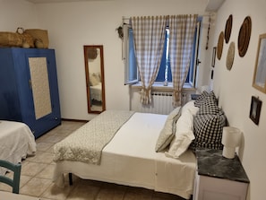 Een slaapkamer met een bed, een blauwe kast, een spiegel, een raam met gordijnen en een radiator.