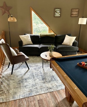 Uma sala de estar aconchegante com sofá seccional, mesa de centro redonda, mesa de bilhar e decoração em formato de estrela na parede.