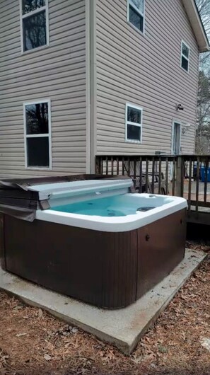 Et spabad i en baghave med en træterrasse og et hus i baggrunden.