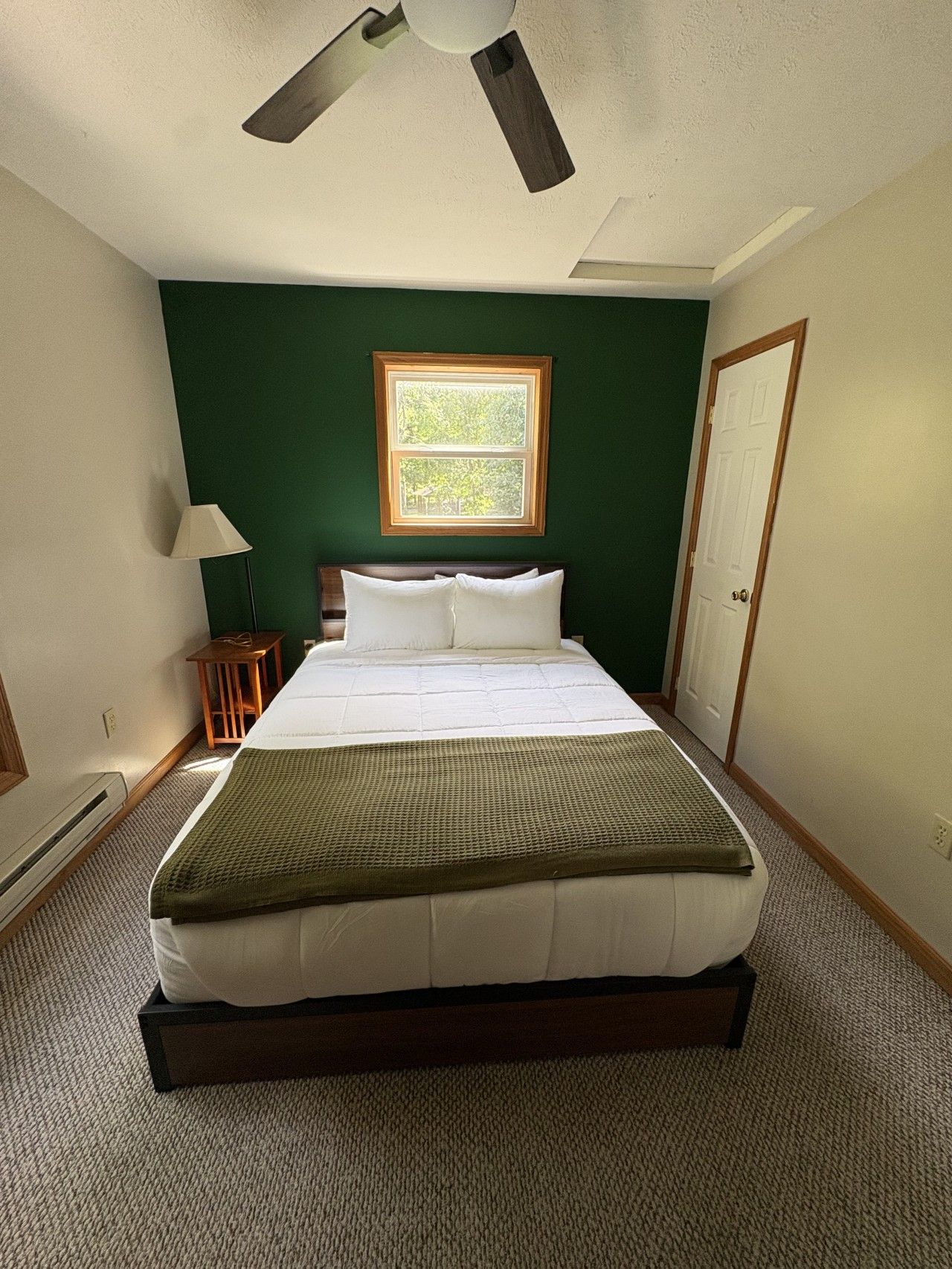 A bedroom with a bed, a window, a door, and a ceiling fan.