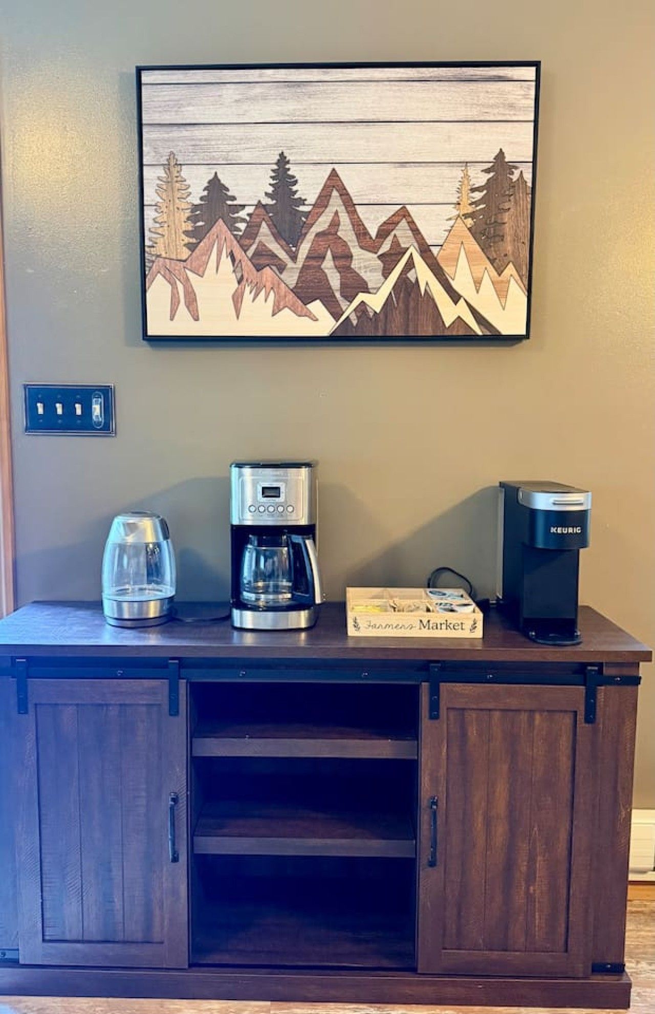 Un mueble de madera con una cafetera, una cafetera Keurig y una caja de cápsulas de café Jergens Market.