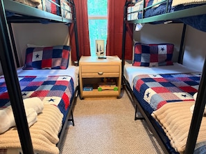 Quarto com beliche, mesa de cabeceira e janela com cortinas.