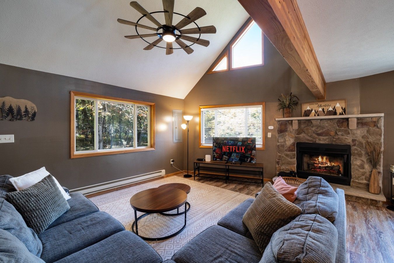 Un salon chaleureux avec une cheminée, une grande fenêtre et un ventilateur de plafond.