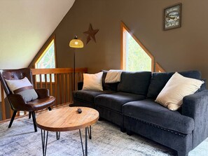 Ein gemütliches Wohnzimmer mit einem Ledersessel, einem dunklen Sofa und einem runden Holztisch.