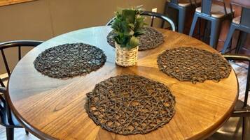 Uma mesa de jantar redonda de madeira com quatro jogos americanos trançados, uma planta em vaso e cadeiras.