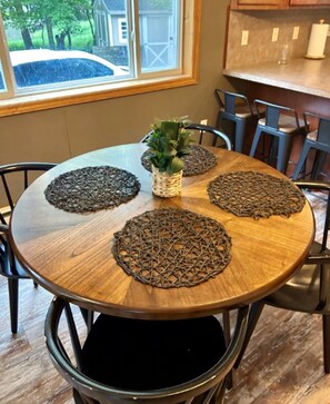 Uma mesa de jantar redonda de madeira com quatro jogos americanos trançados, uma planta em vaso e cadeiras.