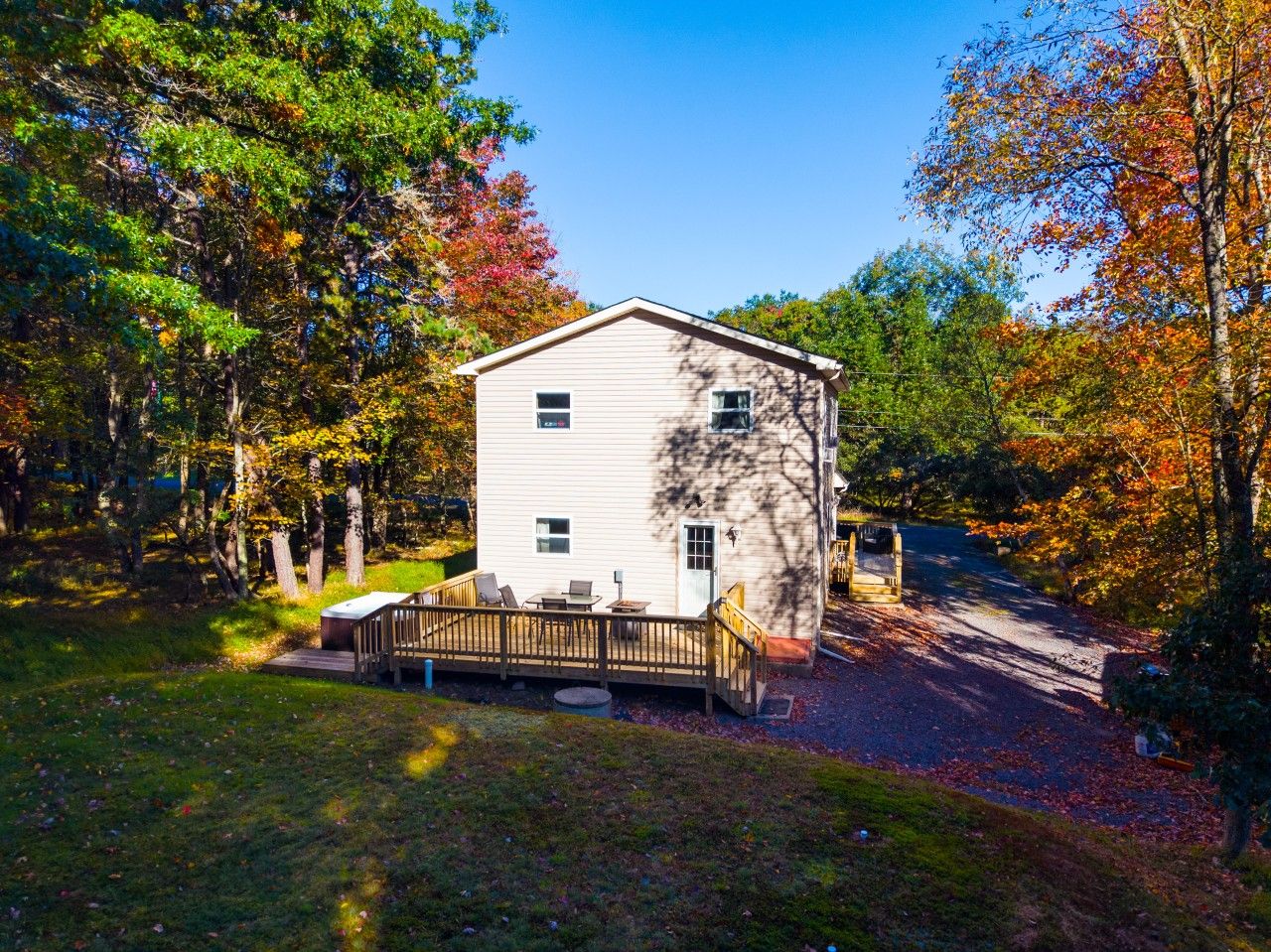 A single-story white building with a deck and a small shed, surrounded by trees with autumn foliage.