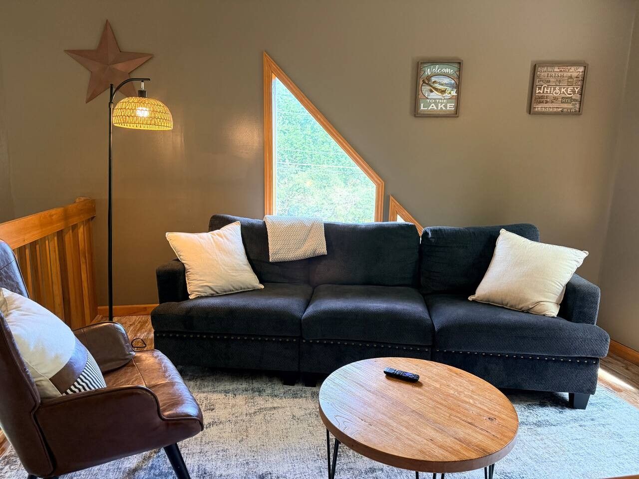 Ein Wohnzimmer mit einem dunkelgrauen Sofa, zwei weißen Kissen, einem Holztisch und einer Wanddekoration in Form eines Sterns.