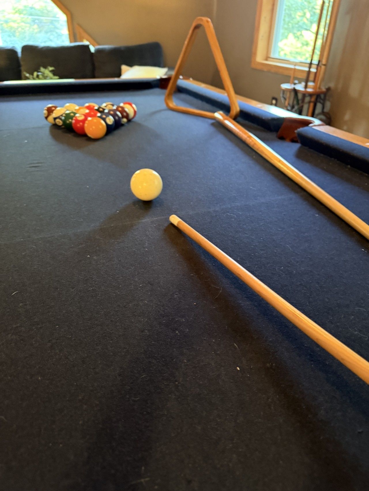 A pool table with a cue stick, billiard balls, and a window in the background.