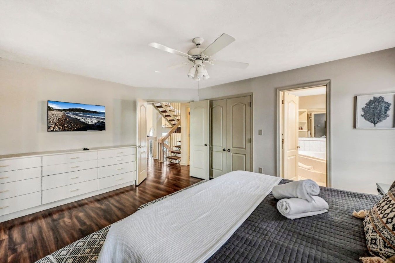 A bedroom with a bed, a ceiling fan, a TV, and a staircase leading to another room.