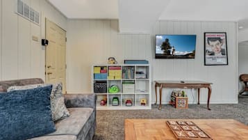 A living room with a sofa, a coffee table, a bookshelf, a television, and a poster on the wall.