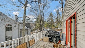 A deck with a grill and chairs, a white railing, and a house with a red door. - Walk 2 Ski: Groups, Kids, Spacious & Well-Stocked (Lake Harmony)