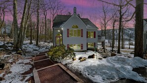 A two-story house with a porch, surrounded by trees and snow. - Walk 2 Ski: Groups, Kids, Spacious & Well-Stocked (Lake Harmony)