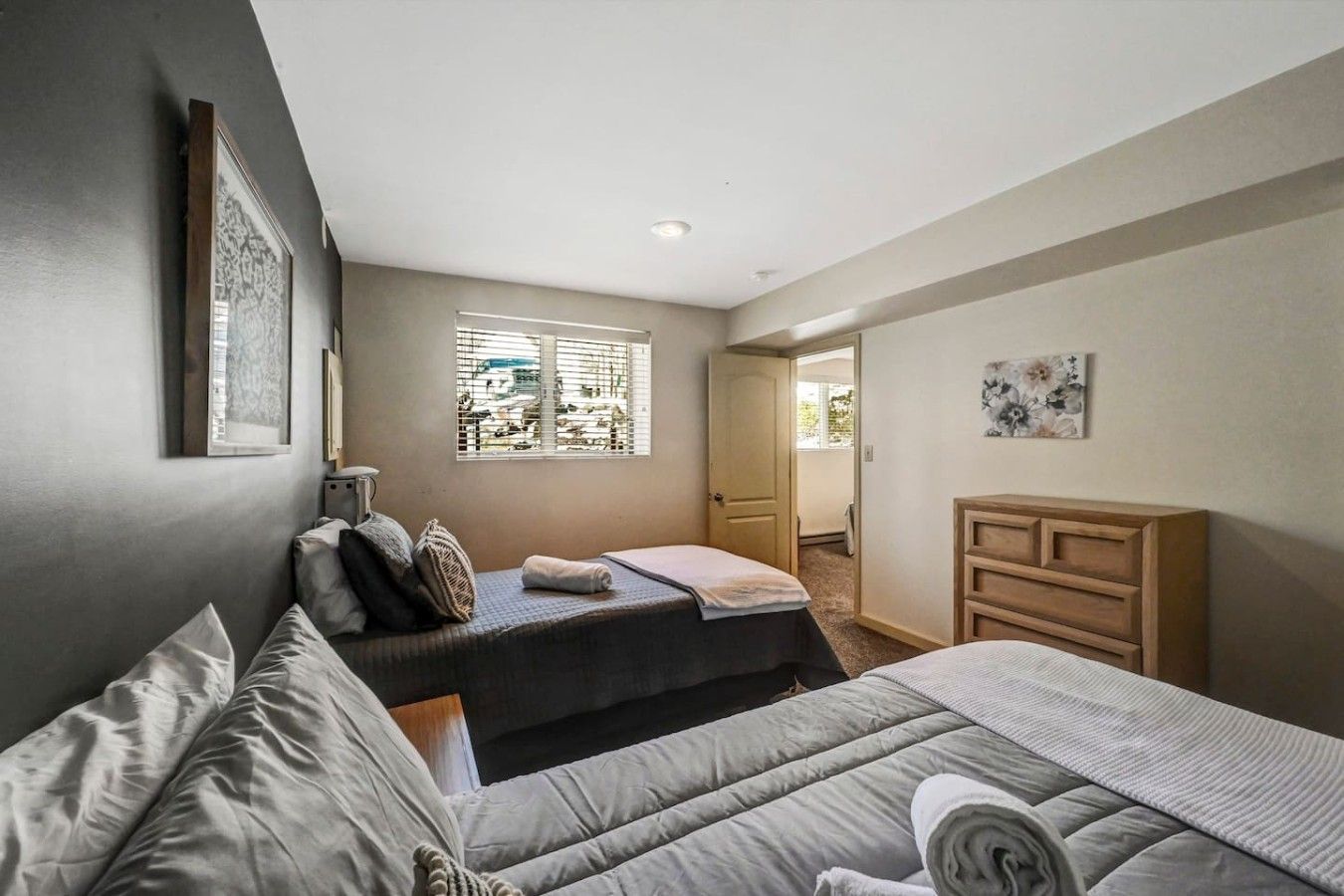 A bedroom with two beds, a wooden dresser, and a window with blinds.