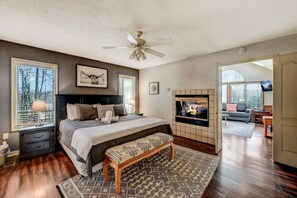 Een slaapkamer met een groot bed, een open haard, een televisie en uitzicht op de omgeving.
